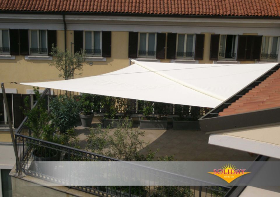 Tenda da sole bianca su un balcone, che fornisce ombra. Edificio sullo sfondo.