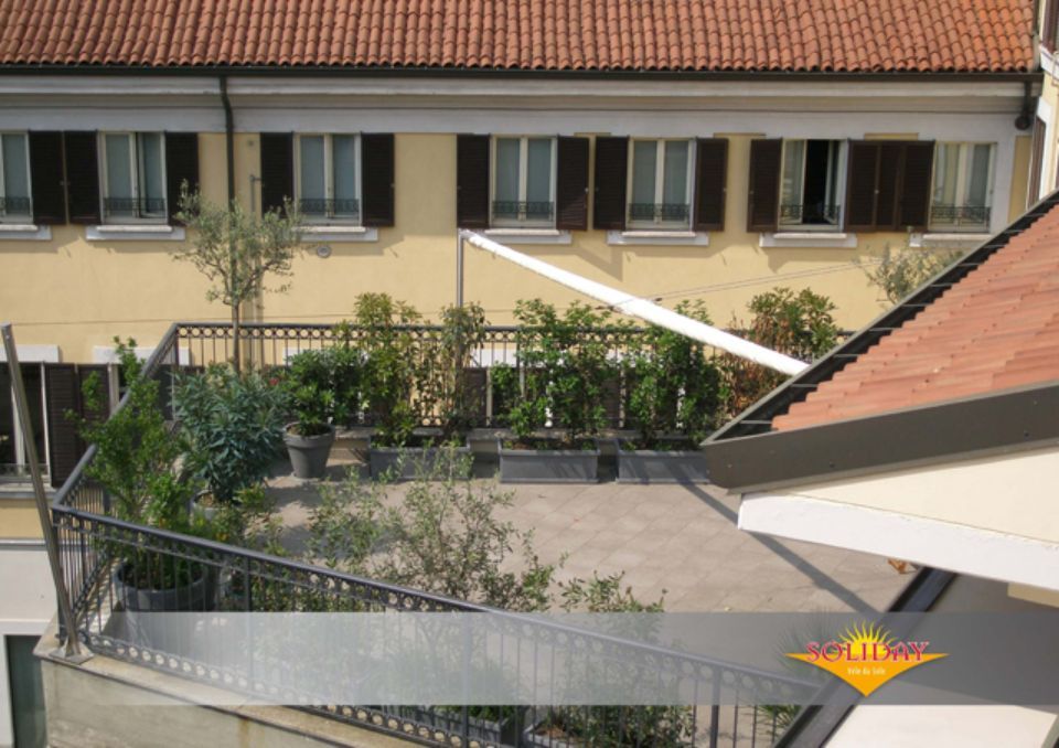 Giardino pensile con ringhiera in metallo, piante e un edificio giallo chiaro con persiane marroni.