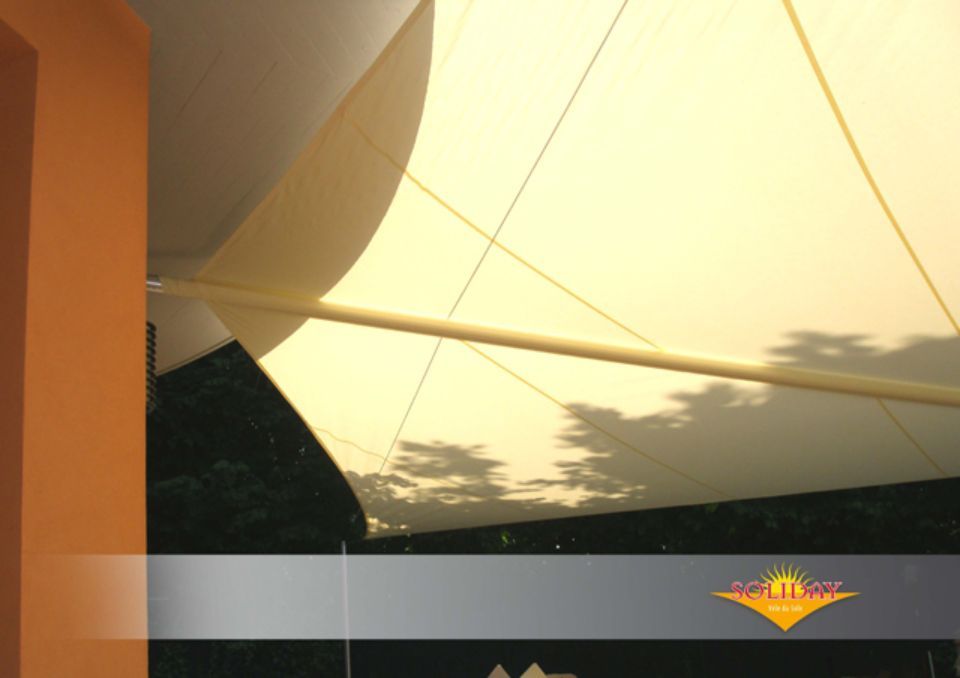 Una grande vela ombreggiante color crema che copre un'area esterna. Proietta ombre e ha un logo dorato in un angolo.