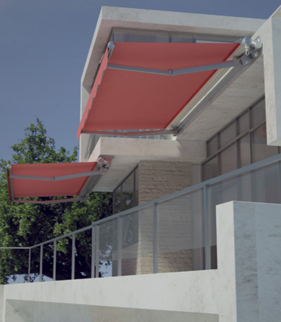 Tende da sole rosse retrattili sul balcone di un edificio moderno, parzialmente estese, che offrono ombra.
