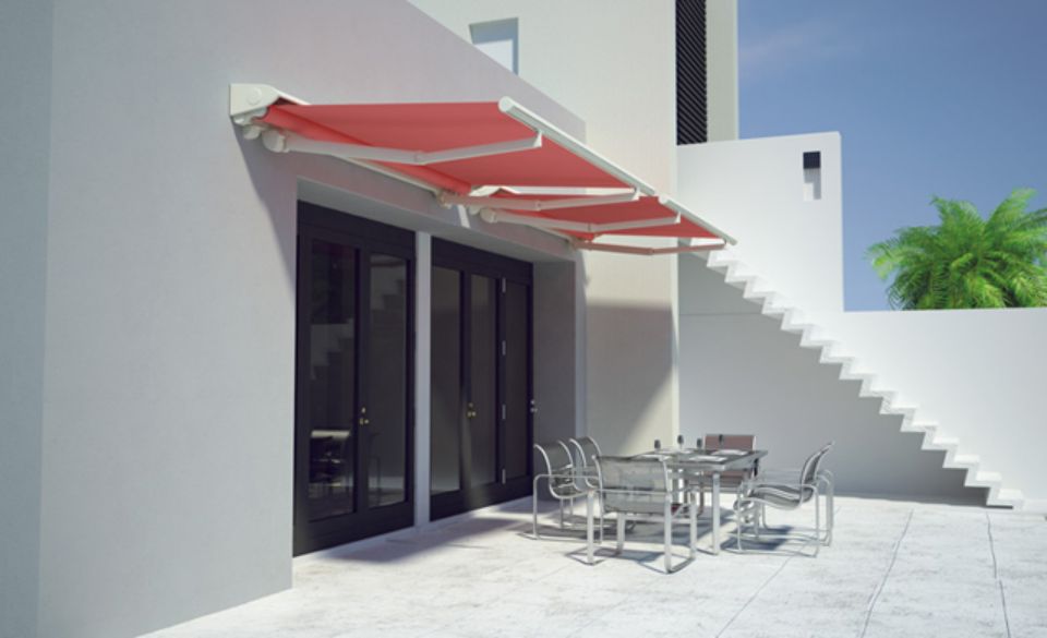 Tenda da sole rossa retrattile sopra una porta a vetri, che ripara i mobili da giardino.