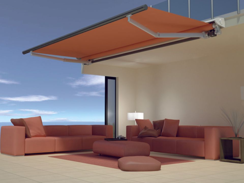 Una tenda da sole arancione ombreggia un patio moderno con divani color corallo e vista sull'oceano.