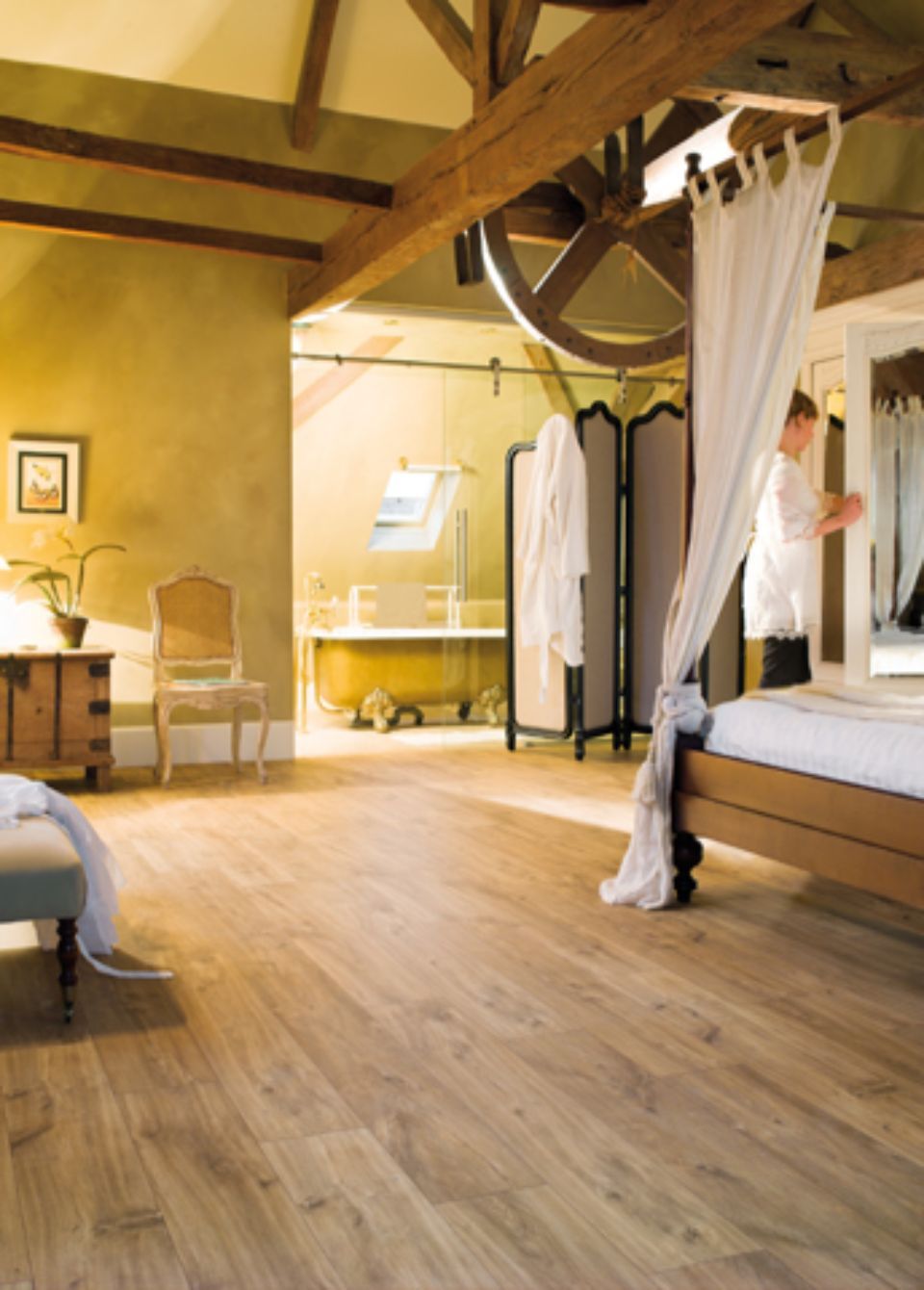 Camera da letto con pavimento in legno, travi a vista, letto a baldacchino, bagno adiacente e persona.