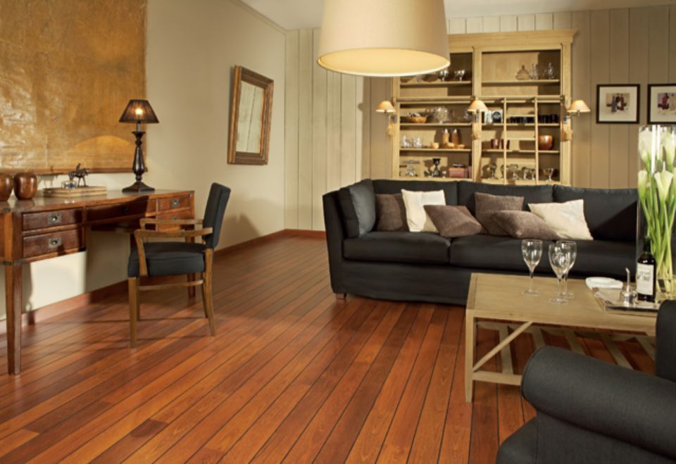 Soggiorno con pavimento in legno, divano nero, scrivania e mobiletto. La luce naturale e i colori neutri.