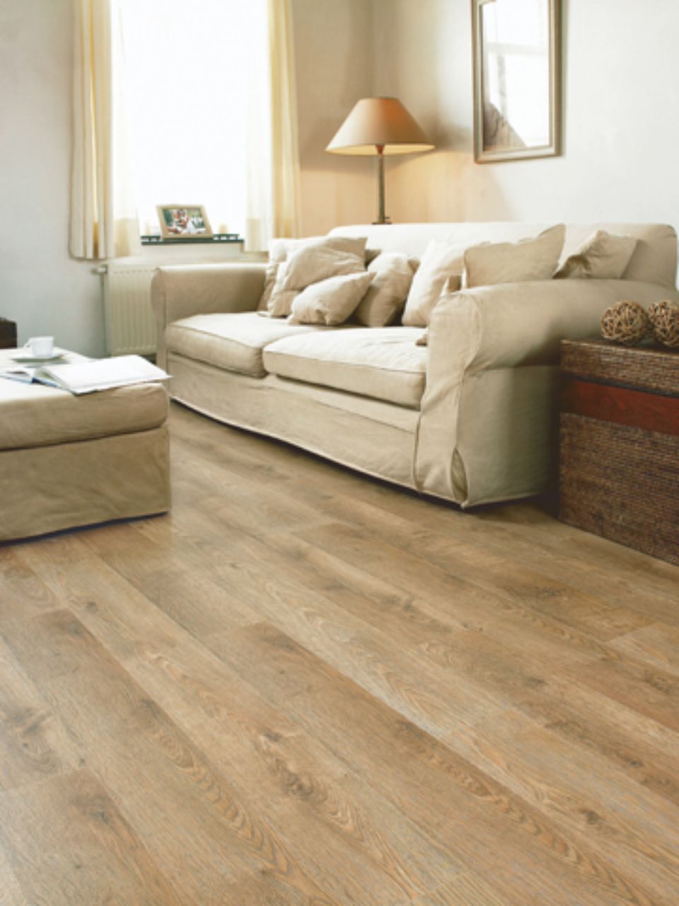 Soggiorno con divano beige, pouf, pavimento in legno e luce naturale proveniente da una finestra.