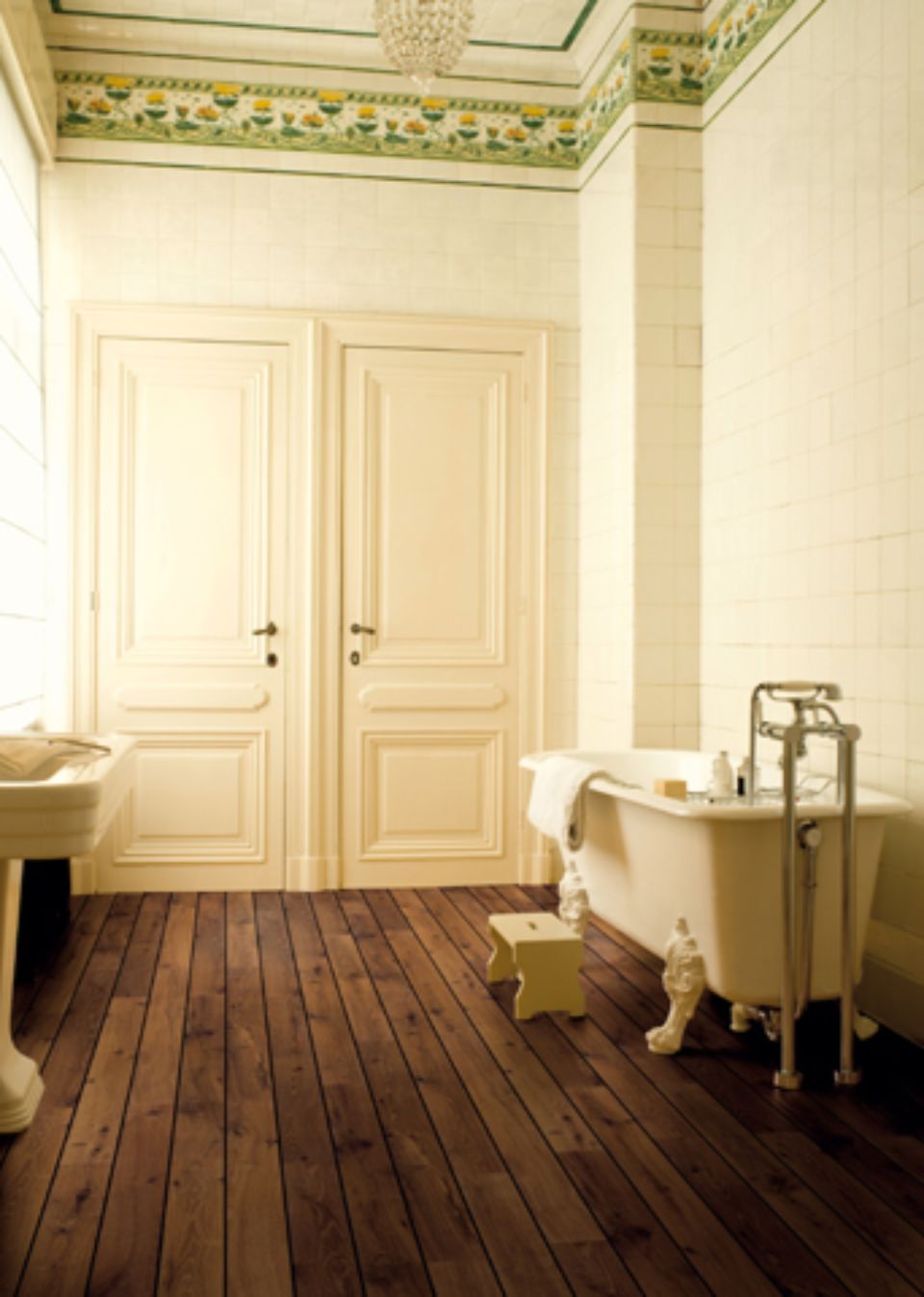 Bagno con vasca con piedini, pavimento in legno, due porte, finiture floreali al soffitto.