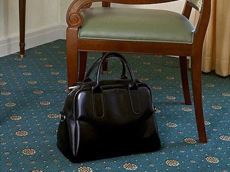 Borsa nera su un tappeto blu fantasia sotto una sedia di legno con seduta verde.