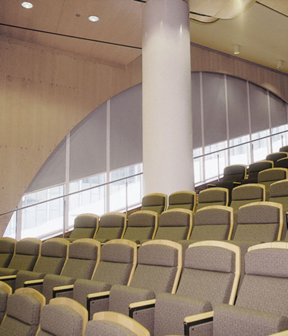File di sedili grigi in un auditorium con finestre ad arco e un pilastro bianco.