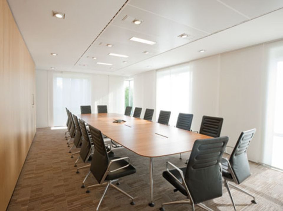 Sala conferenze con lungo tavolo in legno, sedie nere e finestre.