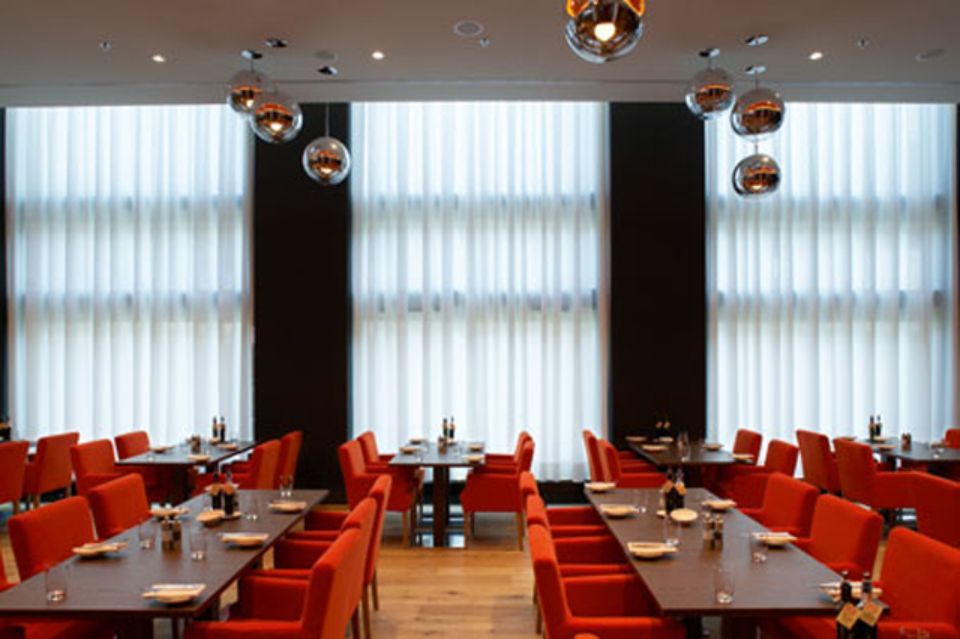 Interno del ristorante con sedie rosse, tavoli scuri, grandi finestre e lampade a globo argentate appese.