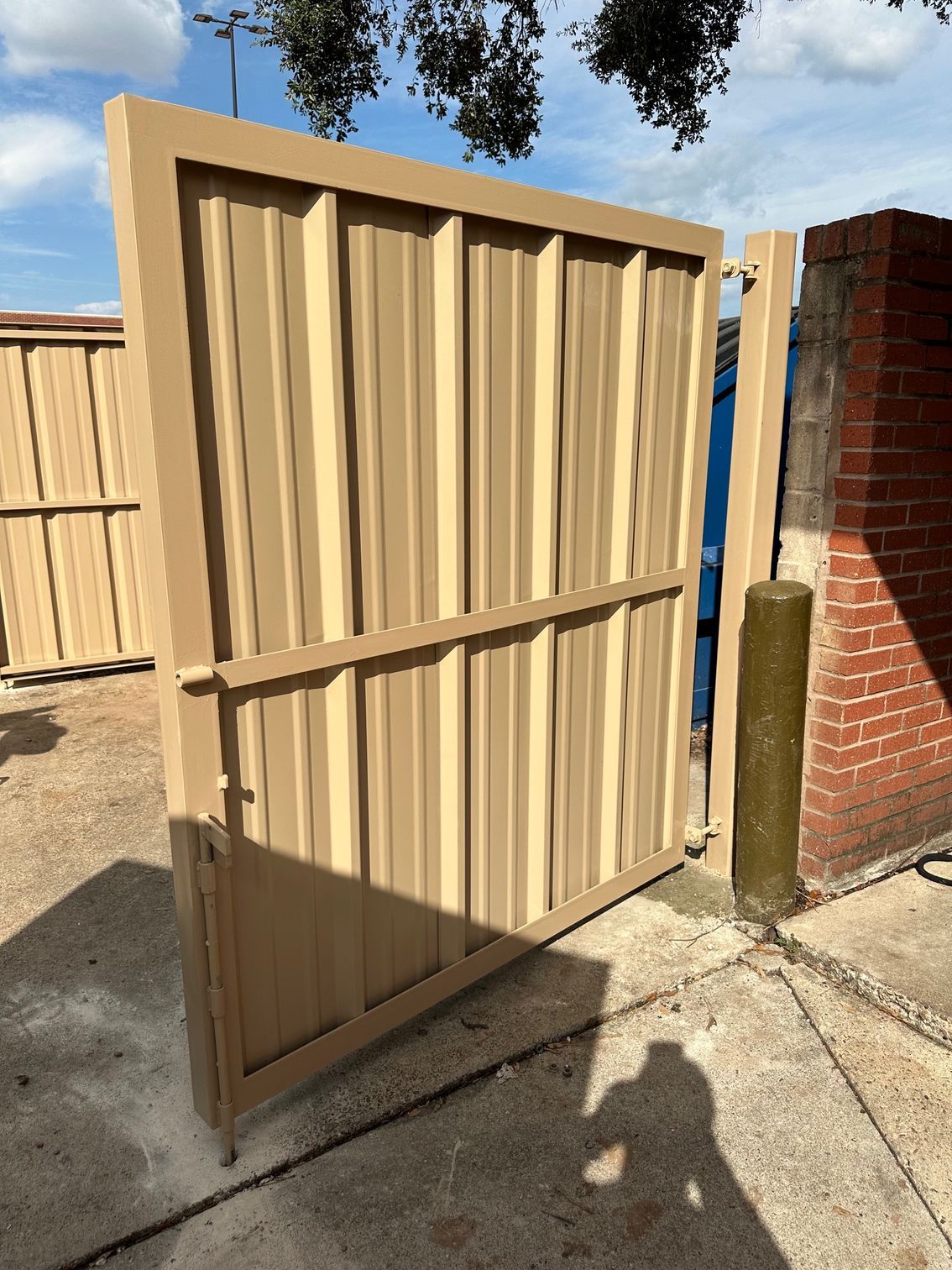 A tan metal gate is sitting on a sidewalk next to a brick wall.