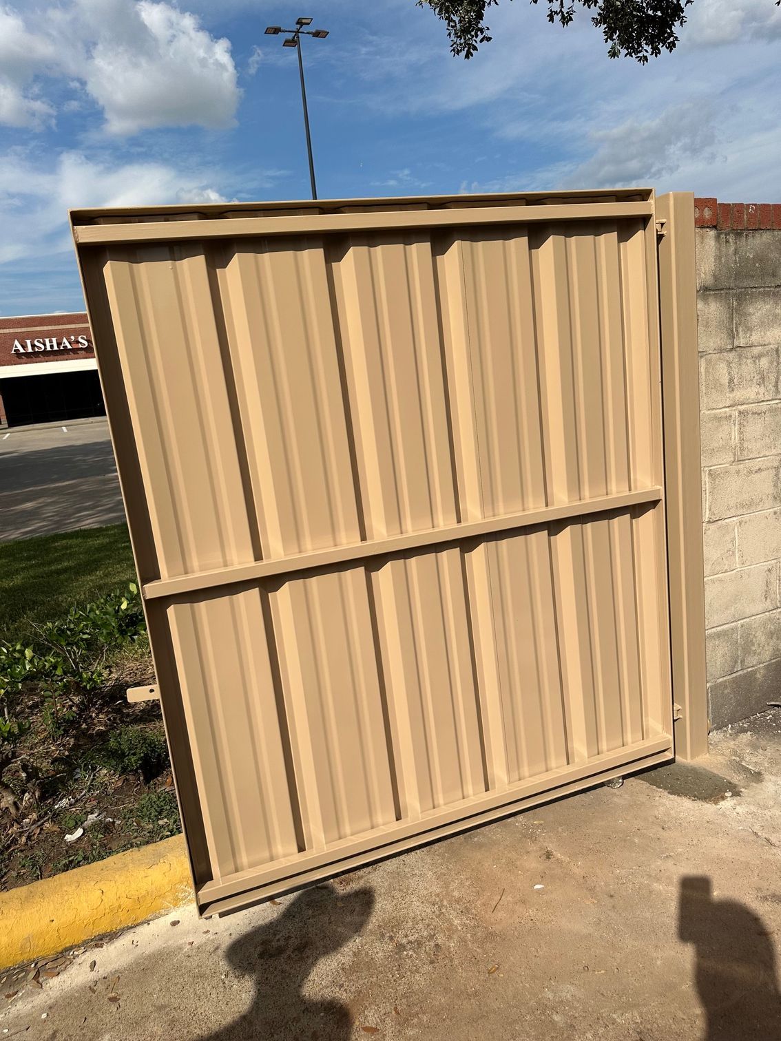 A tan fence is sitting on the side of the road next to a building.