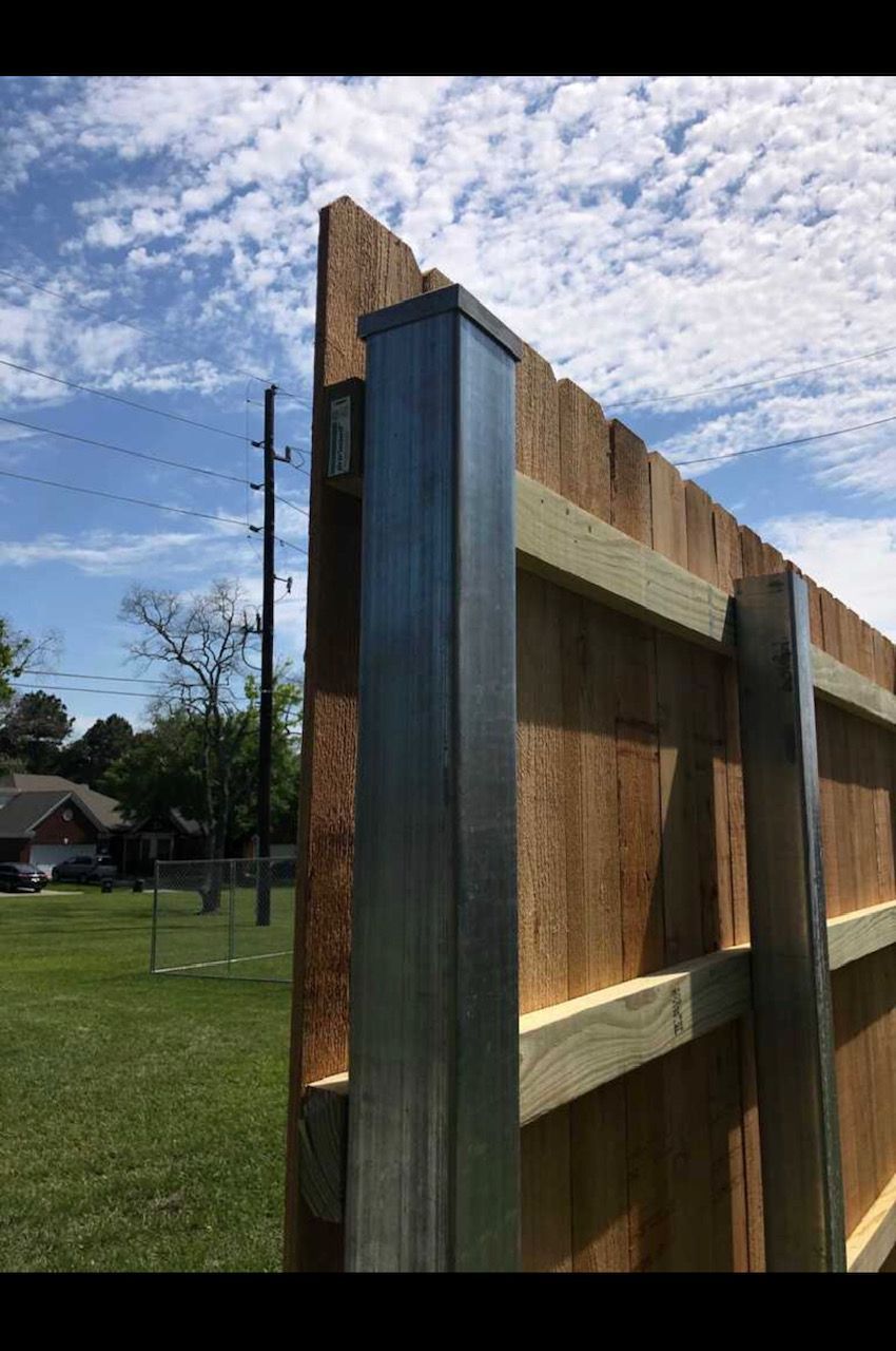 A wooden fence with metal posts is sitting on top of a lush green field.
