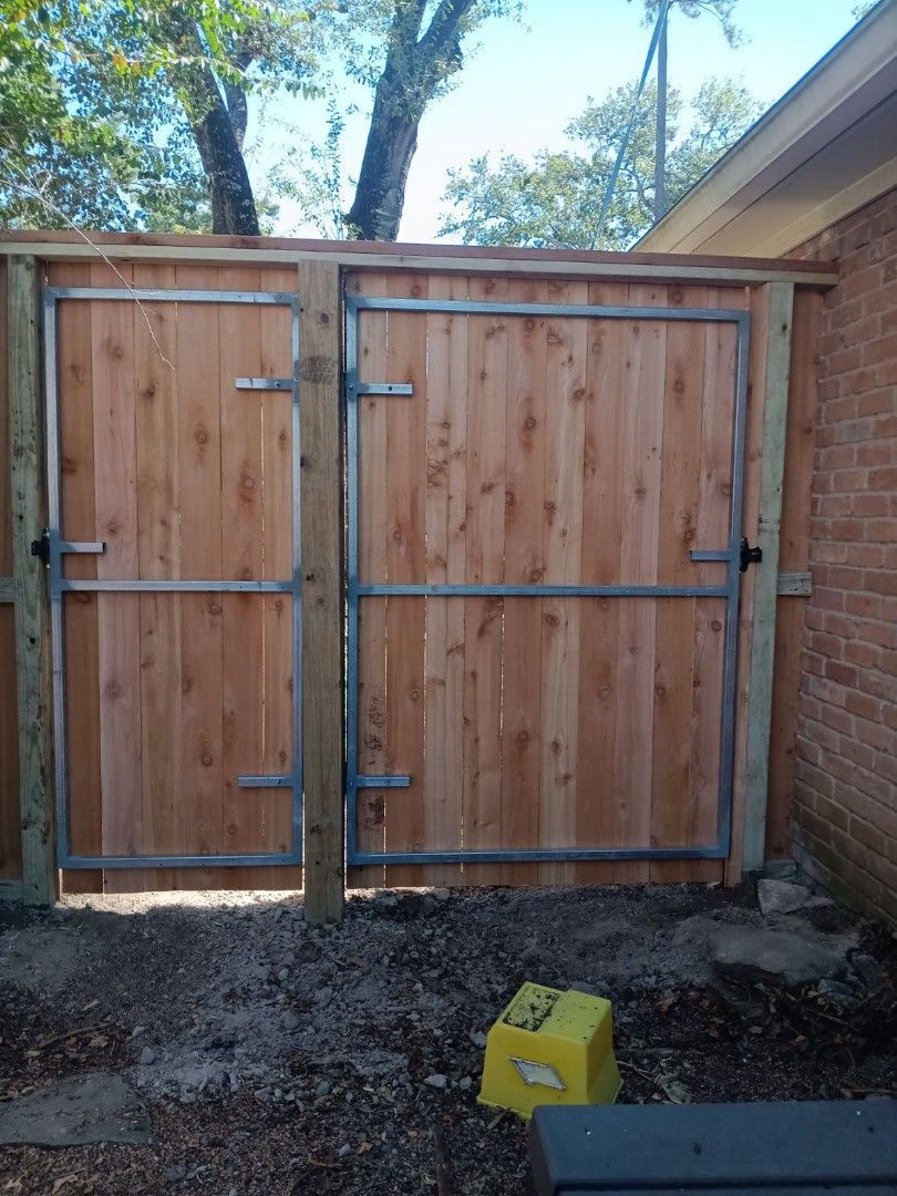 A wooden fence with a metal gate is sitting next to a brick building.