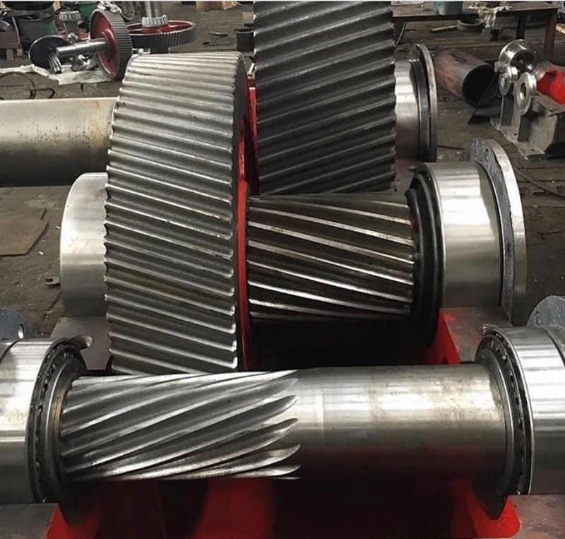 Close-up of large industrial helical gears meshed together on a red metal frame in a factory setting.