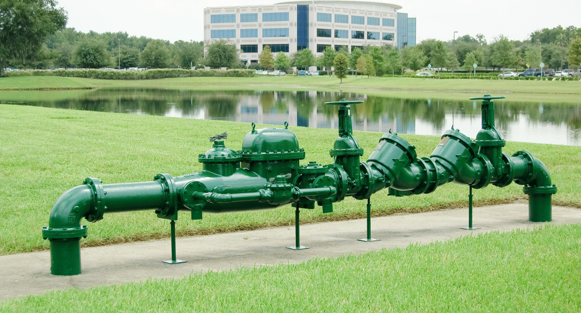 A row of green pipes in a park with a building in the background