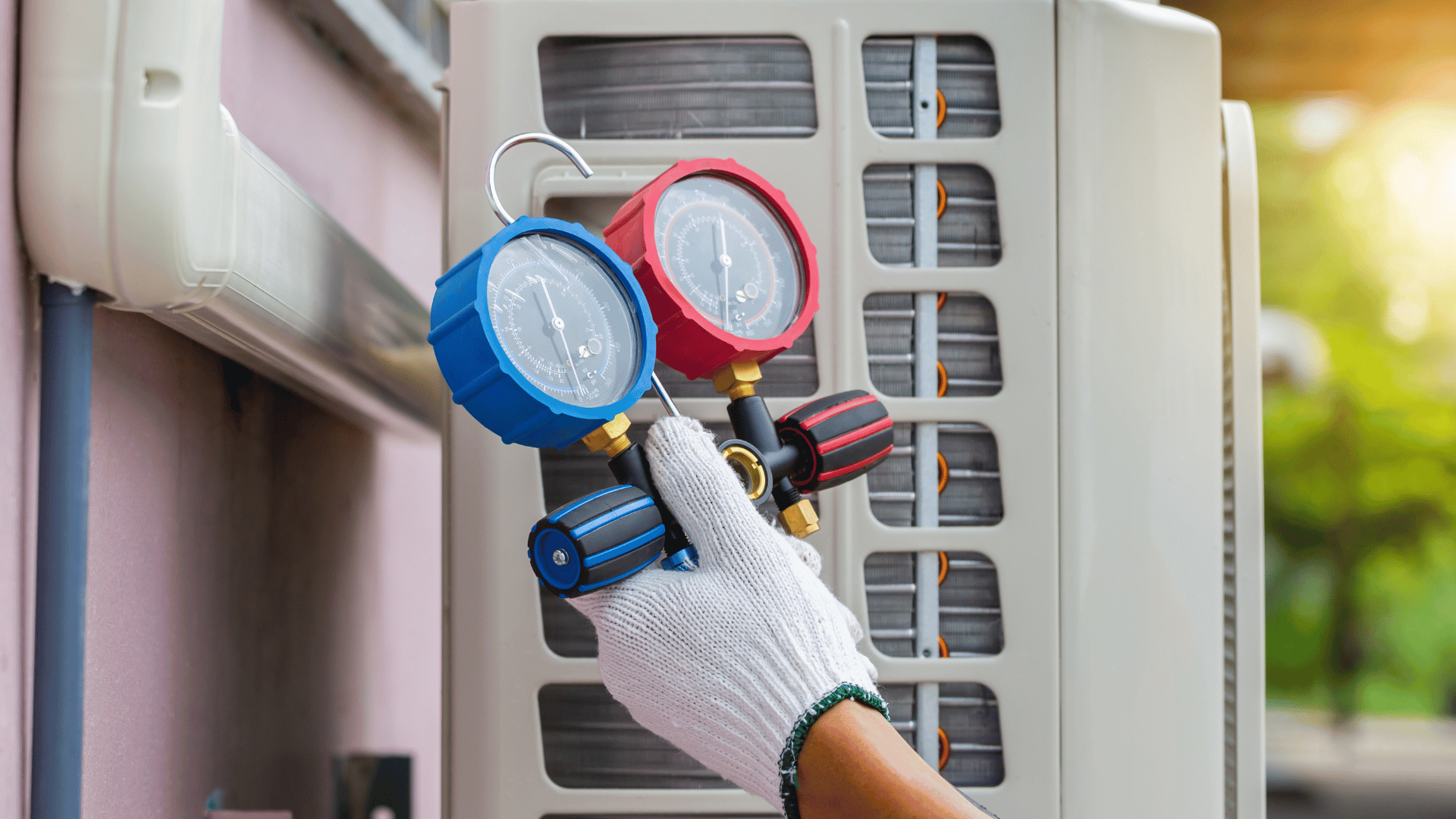 A person is holding two gauges in front of an air conditioner.