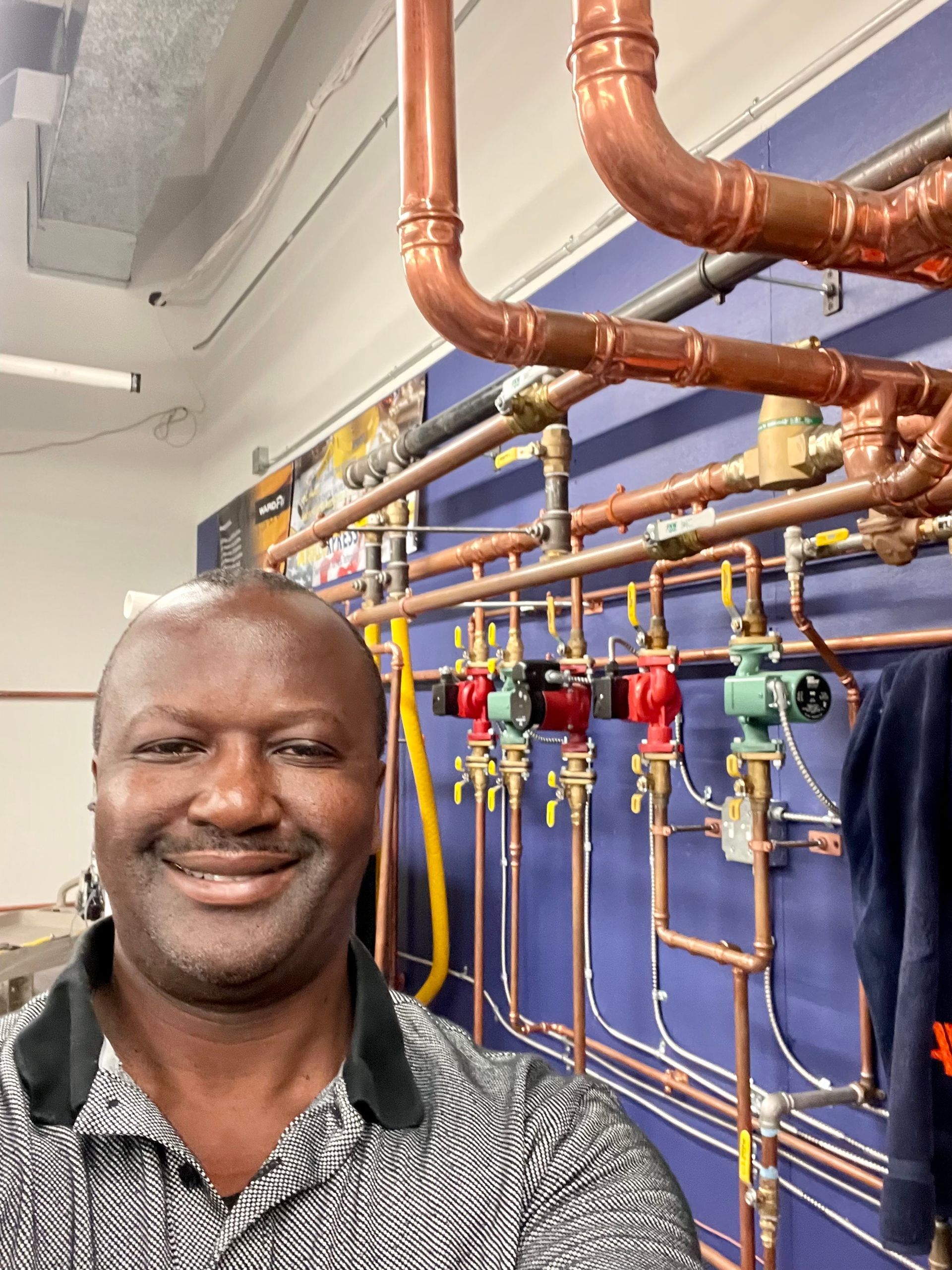 A man is smiling in front of a wall of pipes.
