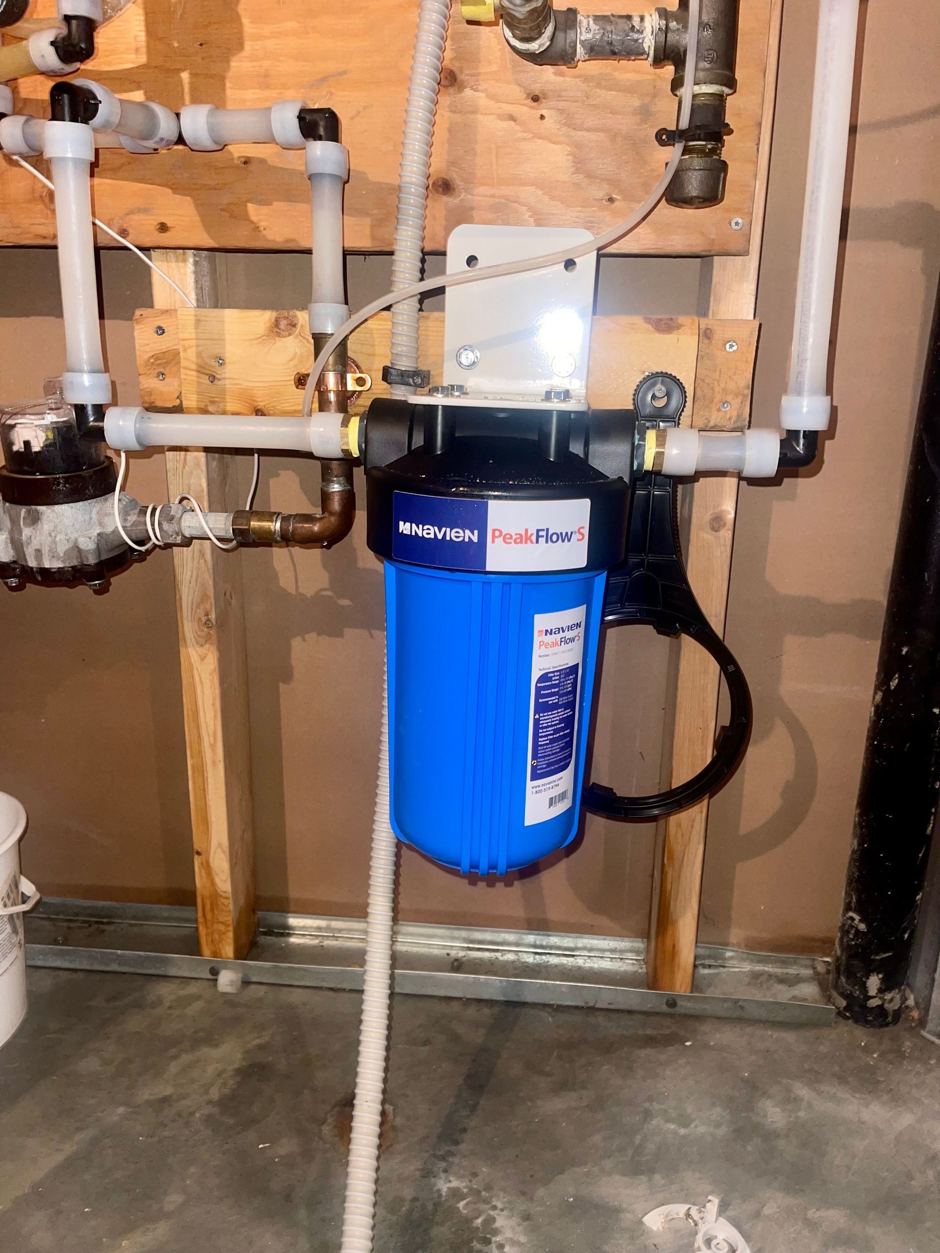 A blue water filter is hanging on a wall next to pipes.