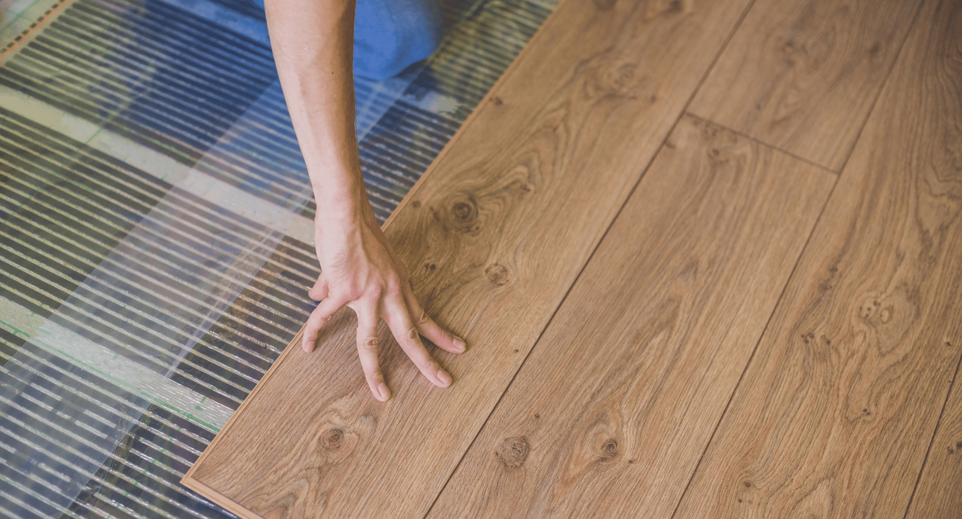 A person is laying a wooden floor on a heated floor.