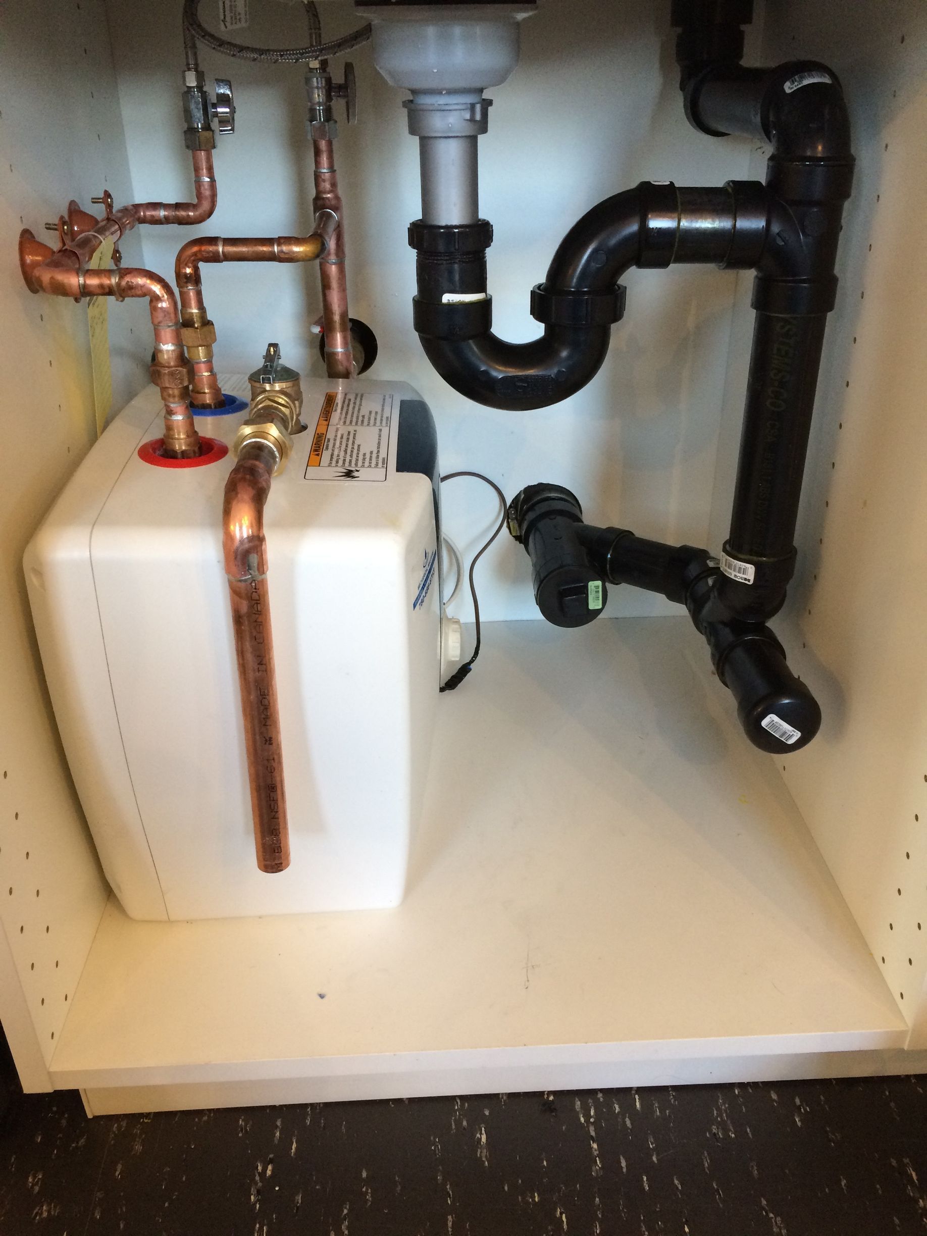 A sink with copper pipes and black pipes underneath it