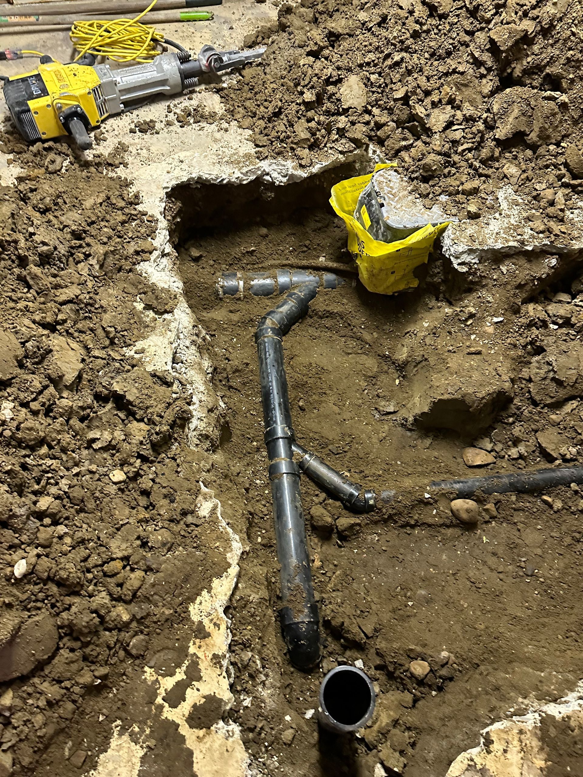 A yellow hammer is sitting on top of a pile of dirt next to a pipe.