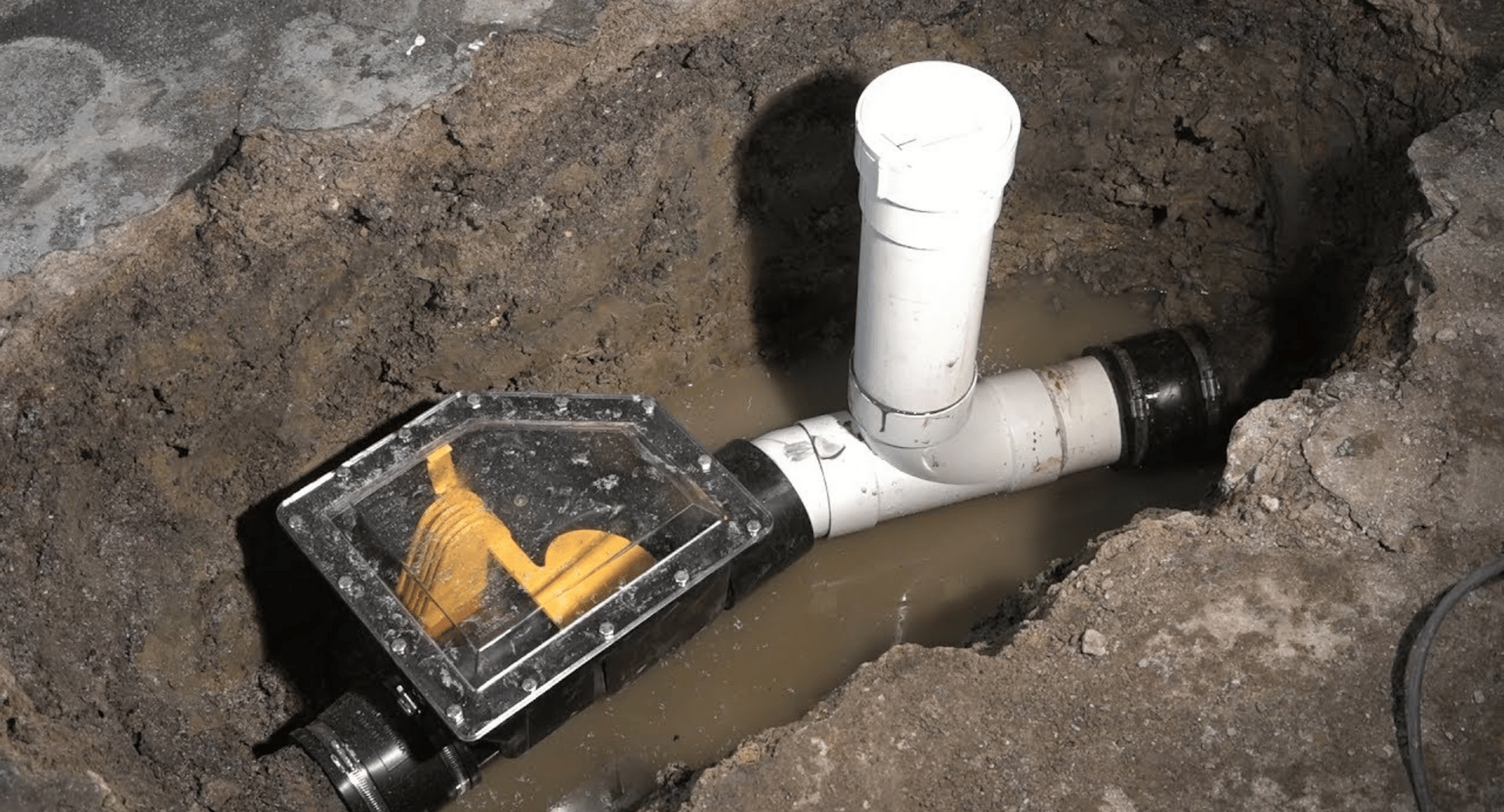 A water meter is sitting in the dirt next to a pipe.
