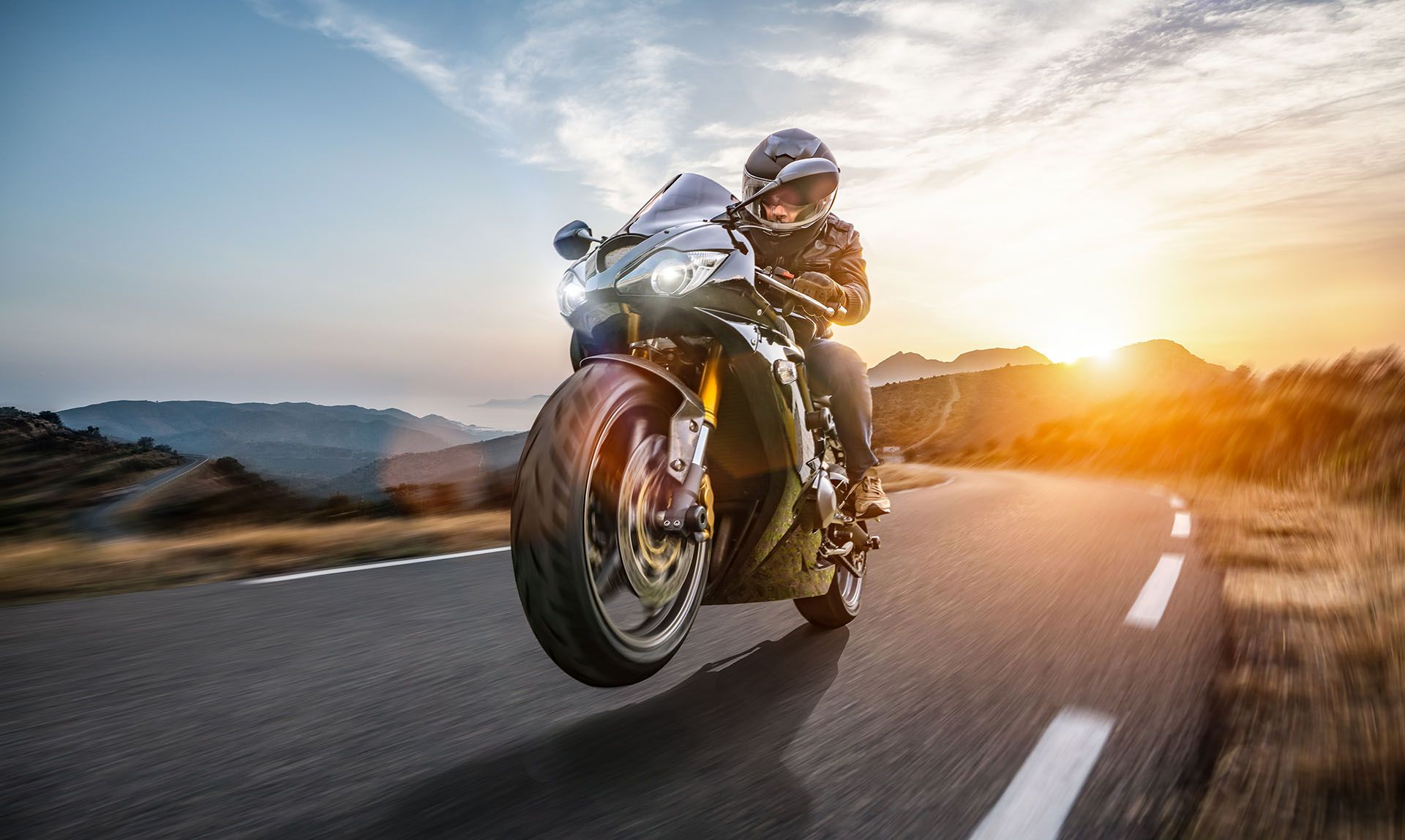 Un motociclista percorre una strada tortuosa al tramonto a bordo di una moto sportiva, con le colline sullo sfondo.