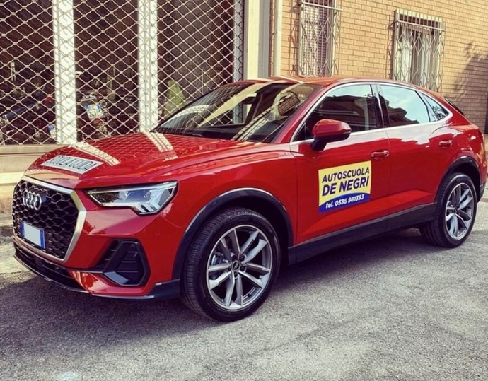 Un'Audi Q3 Sportback rossa parcheggiata davanti a un edificio, con la scritta 