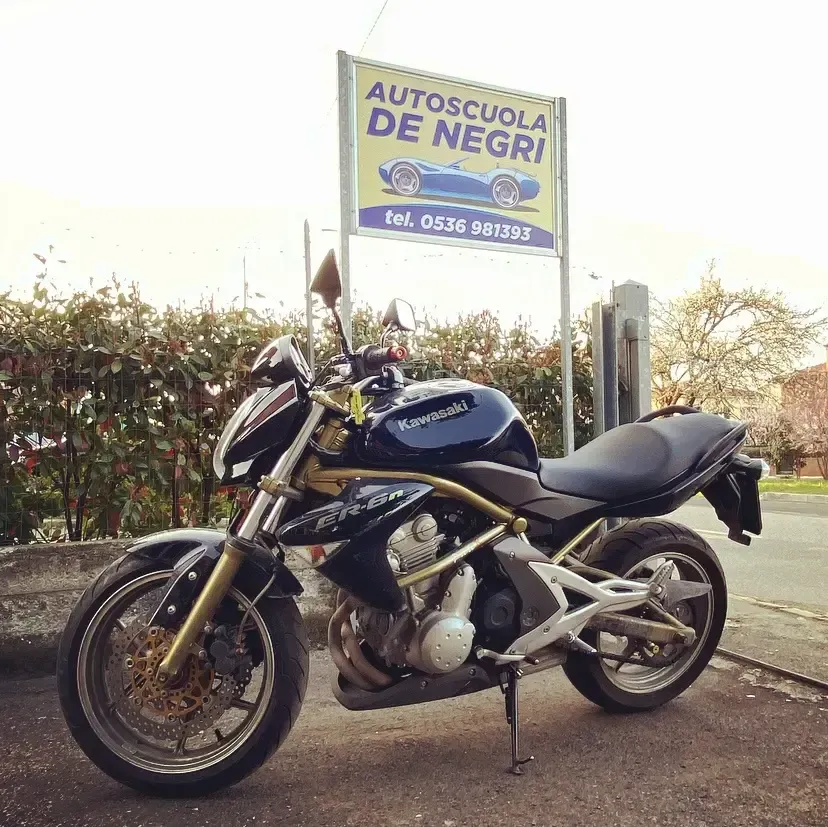 Una motocicletta Kawasaki scura parcheggiata davanti al cartello della scuola guida 