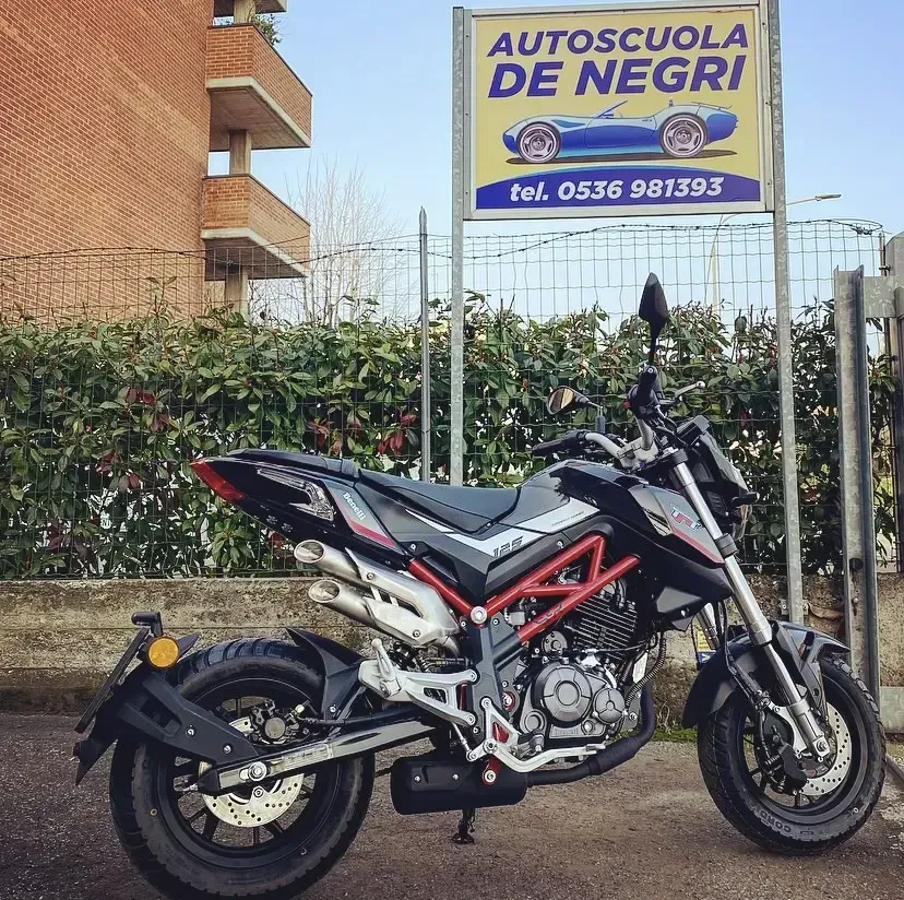 Una motocicletta nera naked con telaio rosso parcheggiata davanti a un cartello giallo della scuola guida 