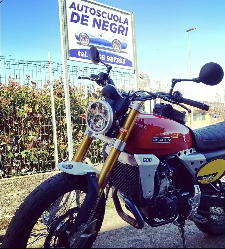 Una motocicletta rossa da 500 cc parcheggiata all'aperto davanti al cartello di una scuola guida.