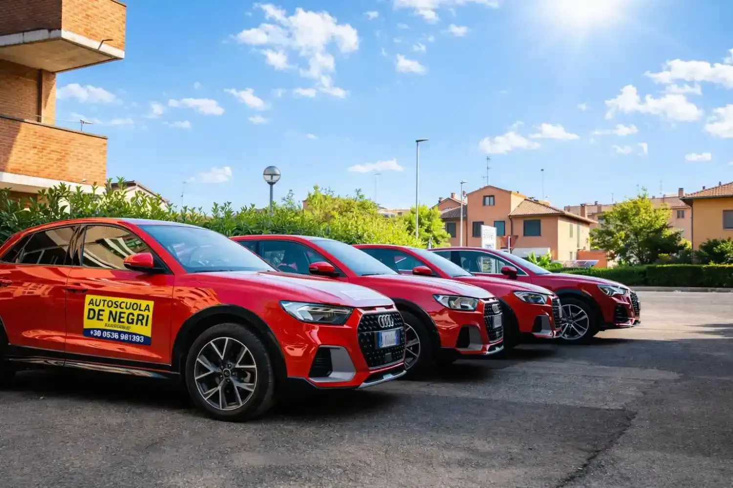 Una motocicletta nera naked con telaio rosso parcheggiata davanti a un cartello giallo della scuola guida 
