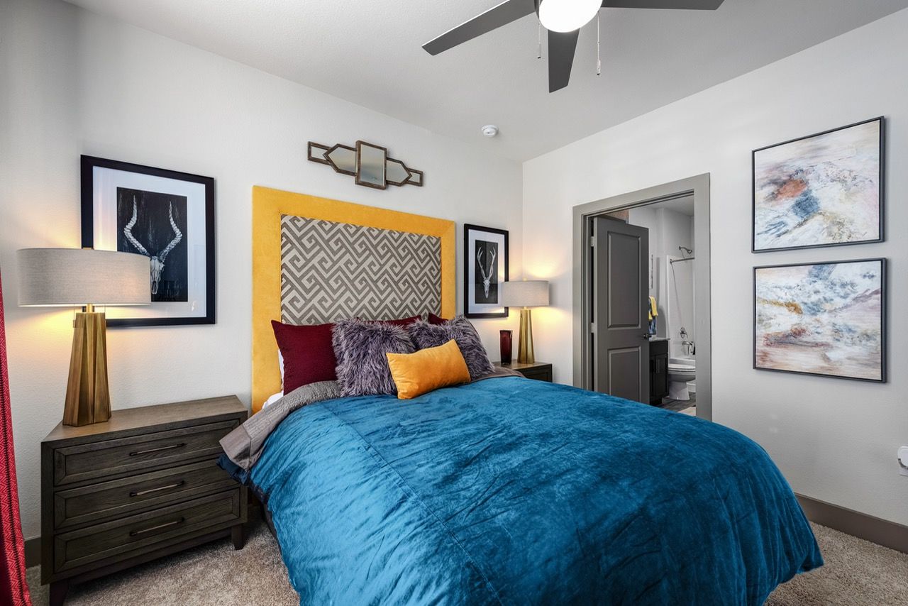 Bedroom in a modern apartment with a blue bedspread, yellow headboard, and nightstands.
