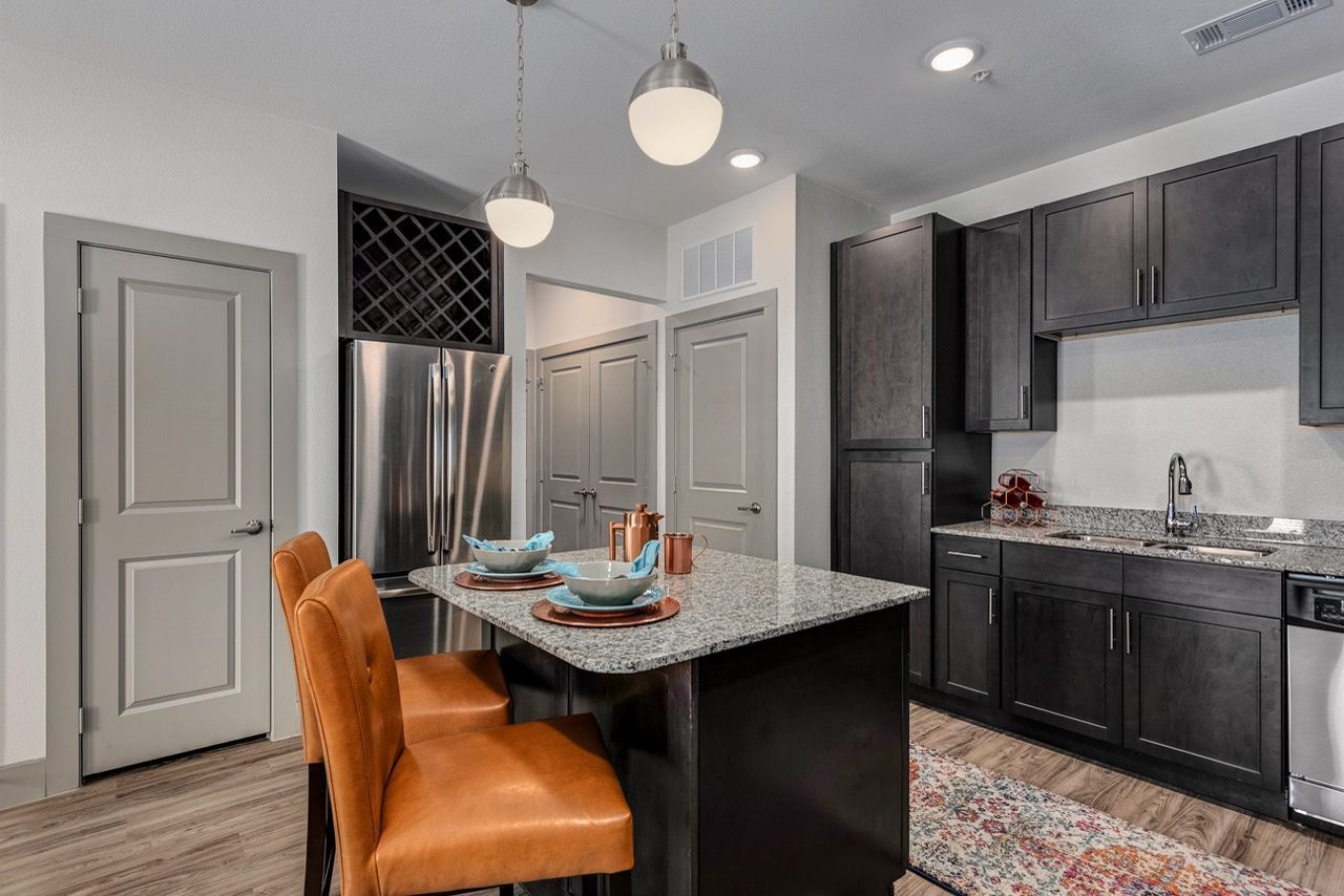 Modern kitchen with granite island, dark cabinets, and stainless-steel appliances.