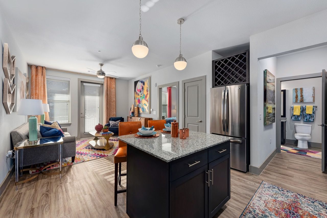 Open-concept apartment living area with island kitchen, sofa, and colorful decor.