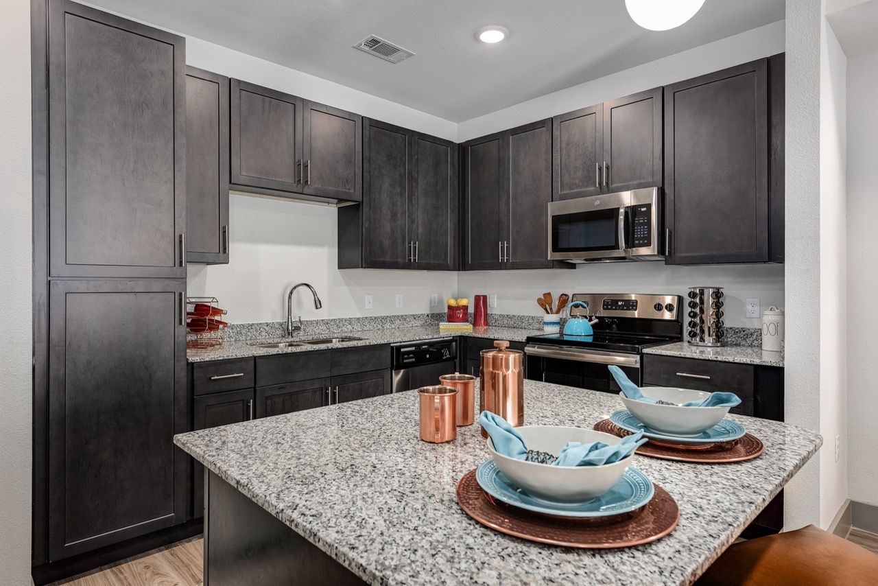 Modern apartment kitchen with dark wood cabinets, granite countertops, and stainless steel appliances.