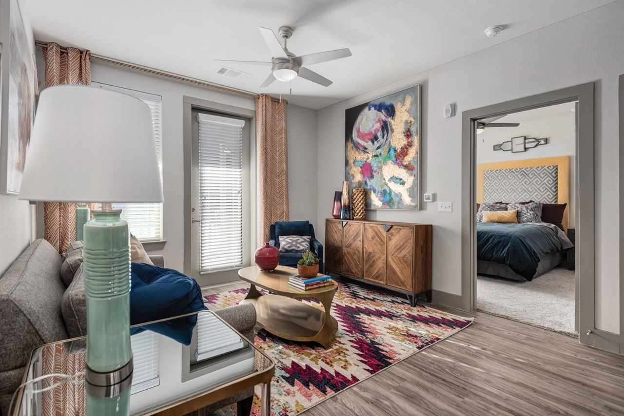 Living room with a gray sofa, a colorful geometric rug, and a doorway to the bedroom.
