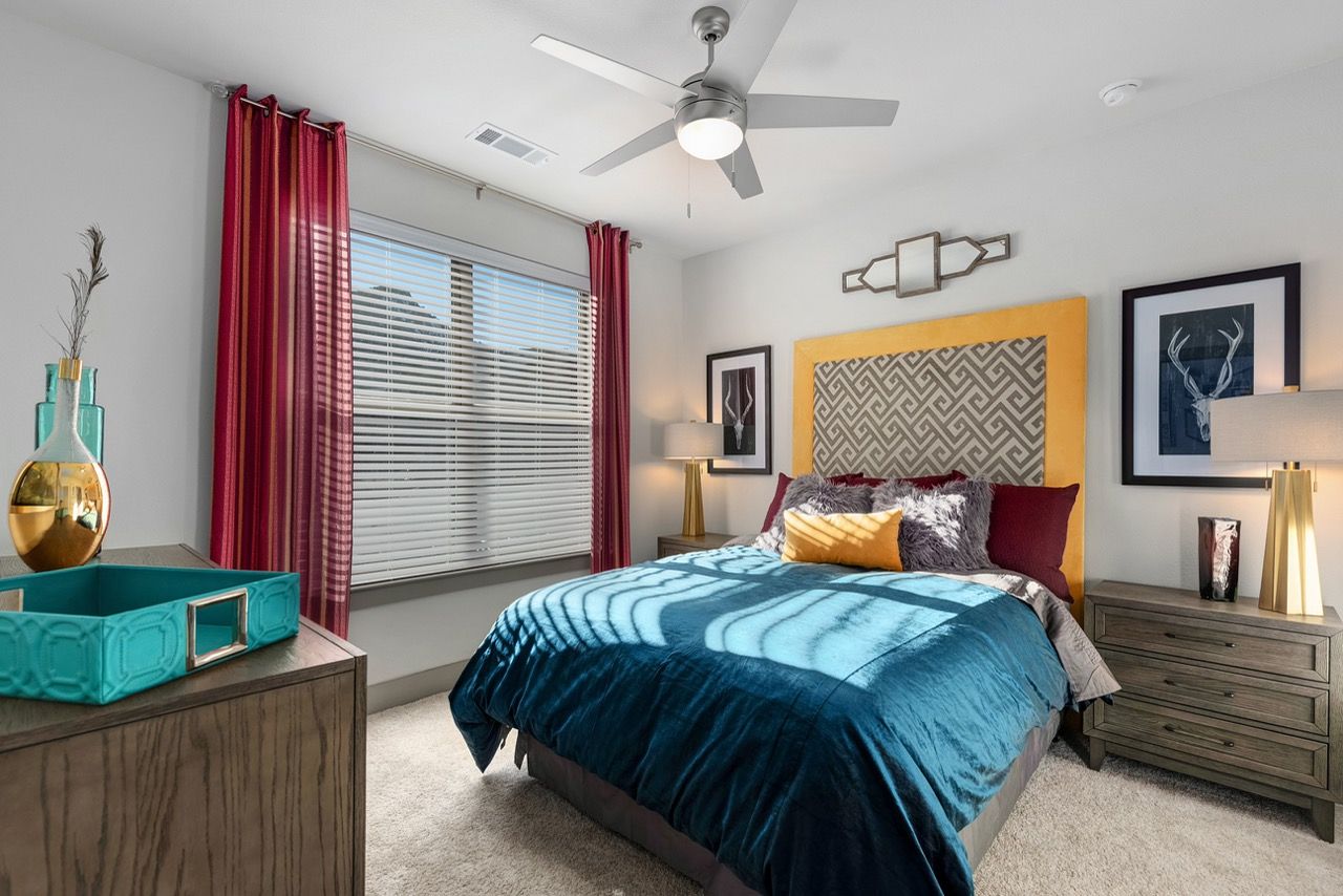 Bedroom in a modern apartment with blue bedding, a yellow headboard, and red curtains.