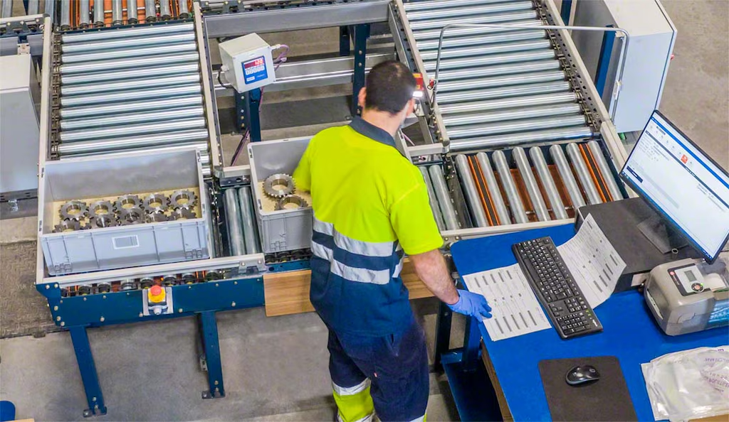 A man is standing in front of a computer in a factory.