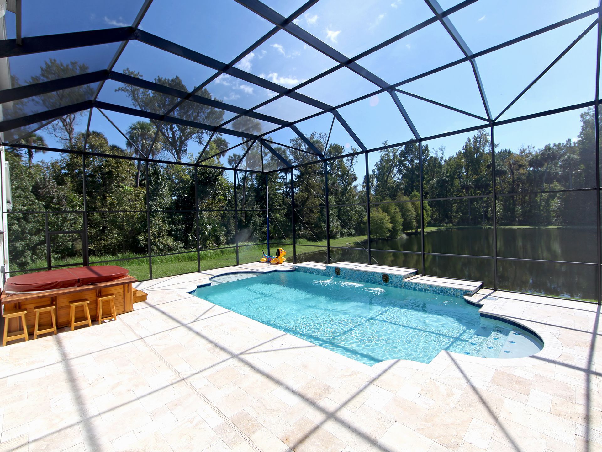 Screened patio with a swimming pool, hot tub, and view of trees and a pond.