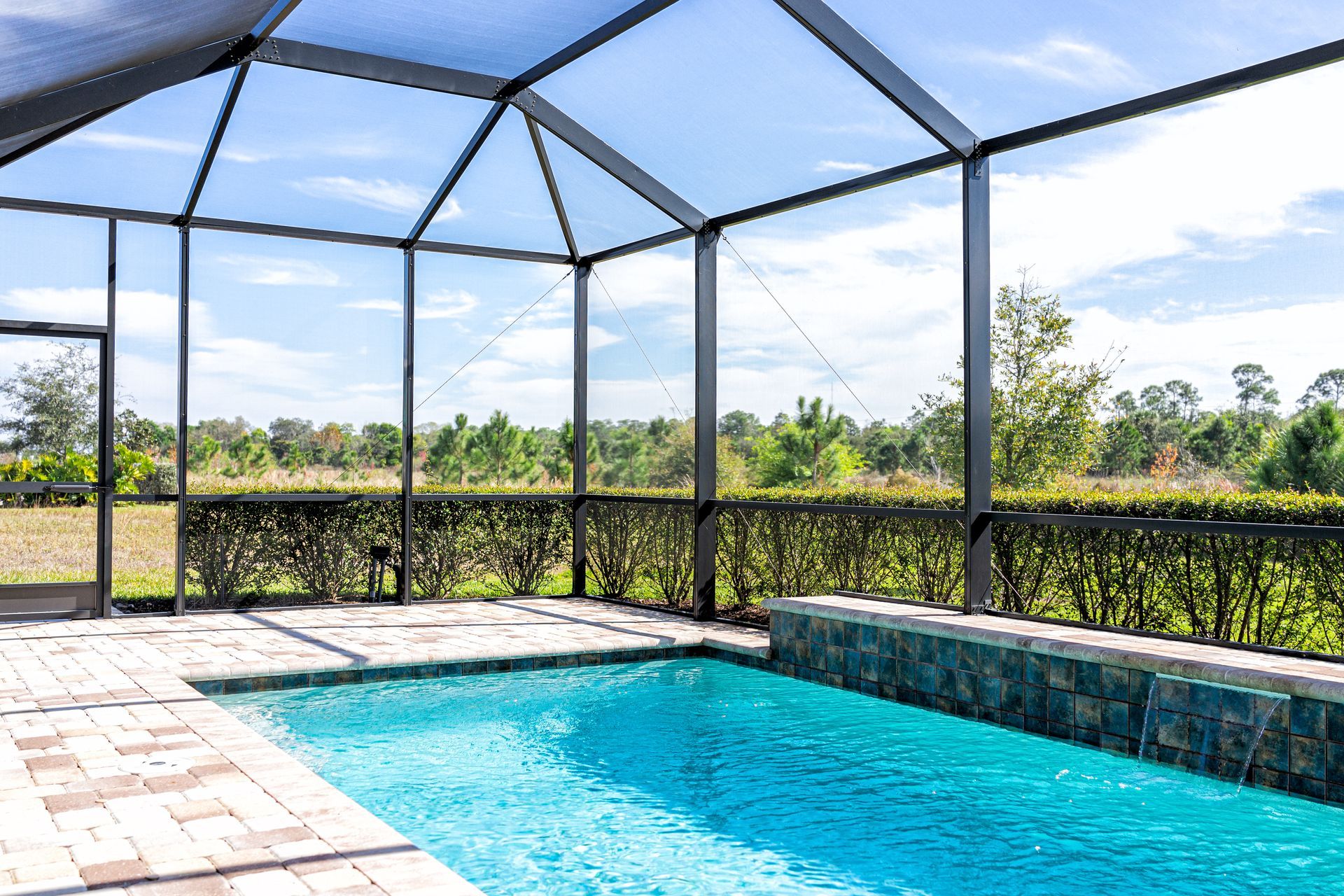 A screened outdoor pool area with clear blue water overlooking trees and open greenery.