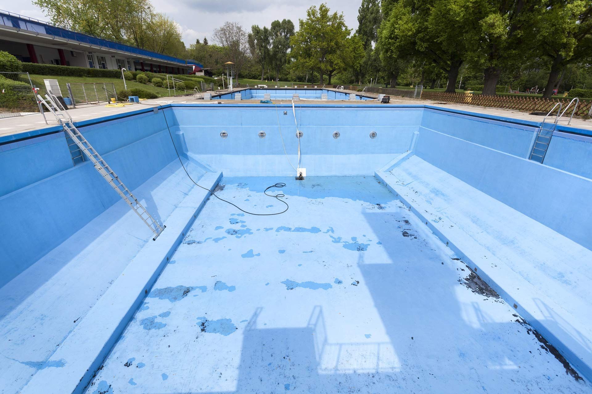 An empty blue swimming pool with trees in the background