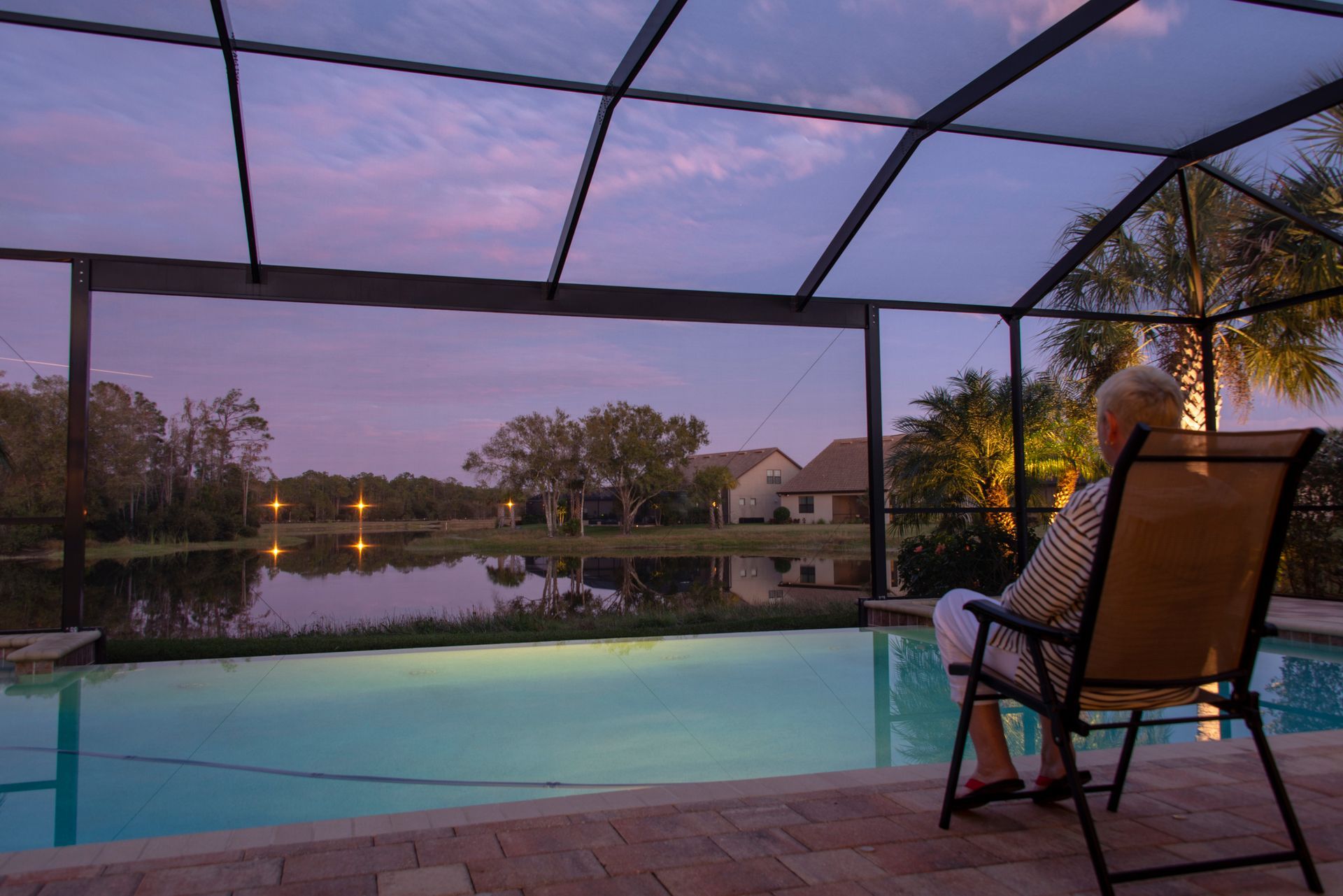 Pool screen enclosure overlooking lake at sunset with patio seating.