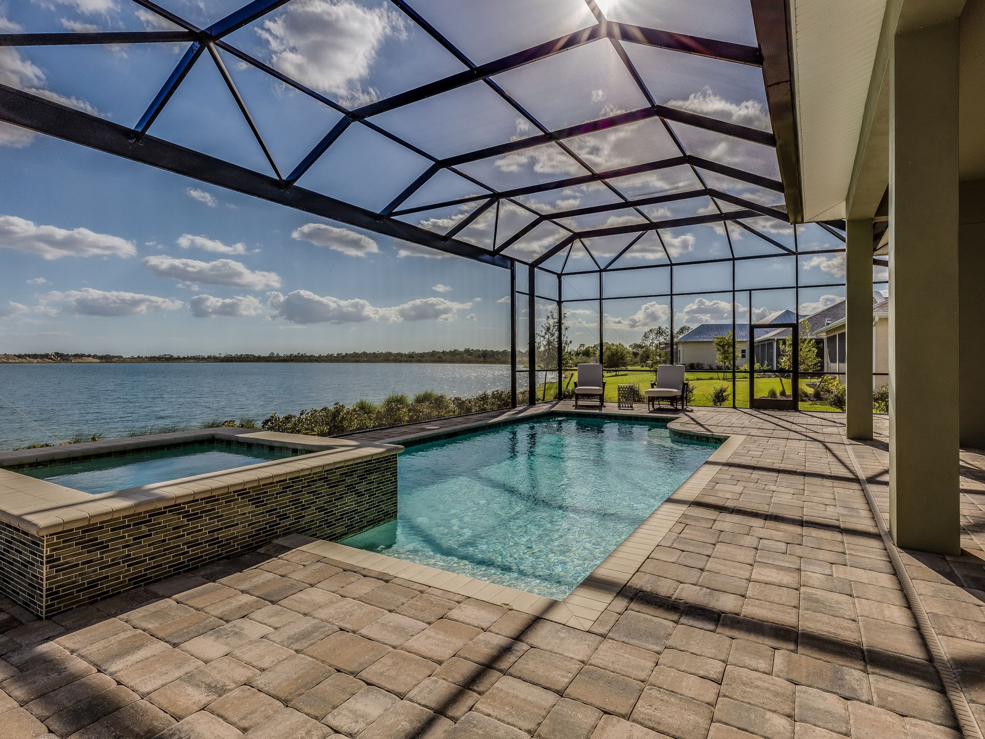 Residential screen enclosure around backyard pool with lake view and patio furniture.