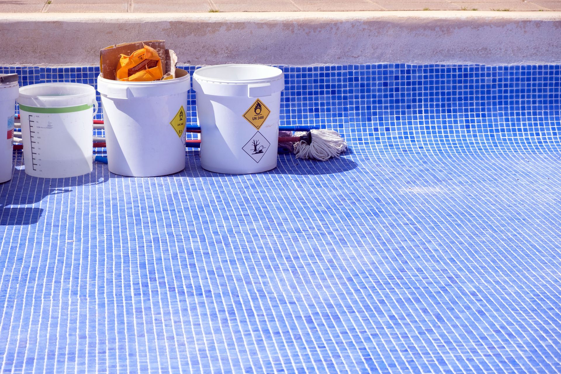 Buckets with chemical labels in an empty tiled pool.