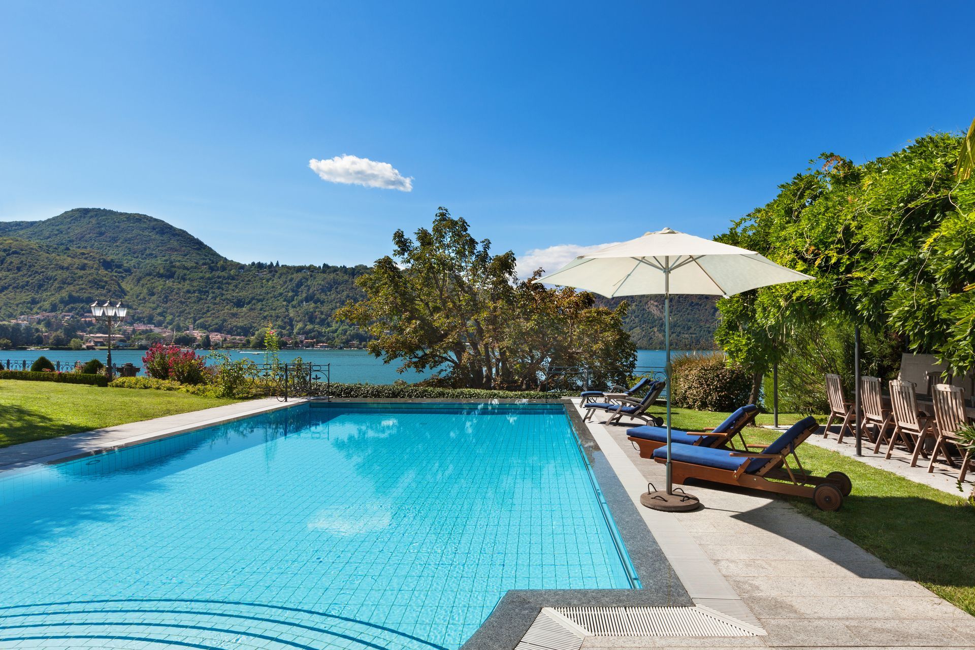 Swimming pool with lounge chairs, umbrella, and lake view under a blue sky.