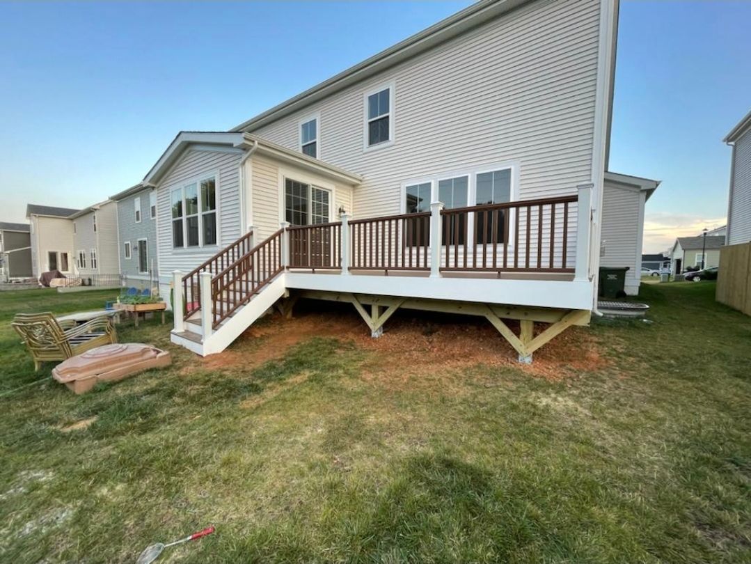 Back of two-story house with a wooden deck; brown railings, white siding, and green grass.