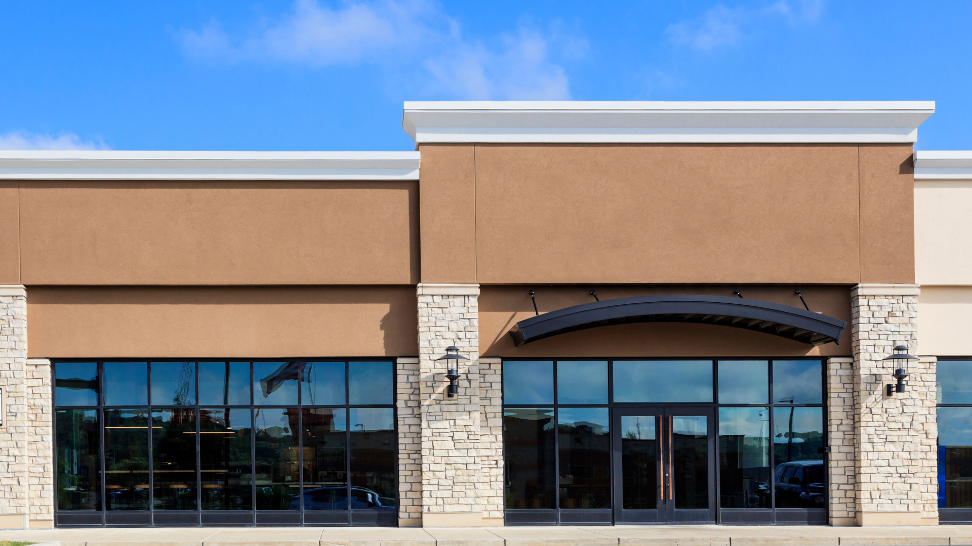 Empty storefront with large glass windows and tan facade under a blue sky