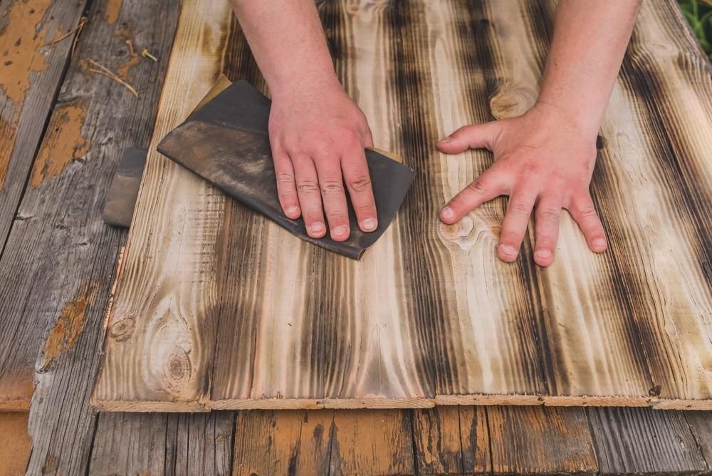 A person is sanding a piece of wood with a sandpaper.